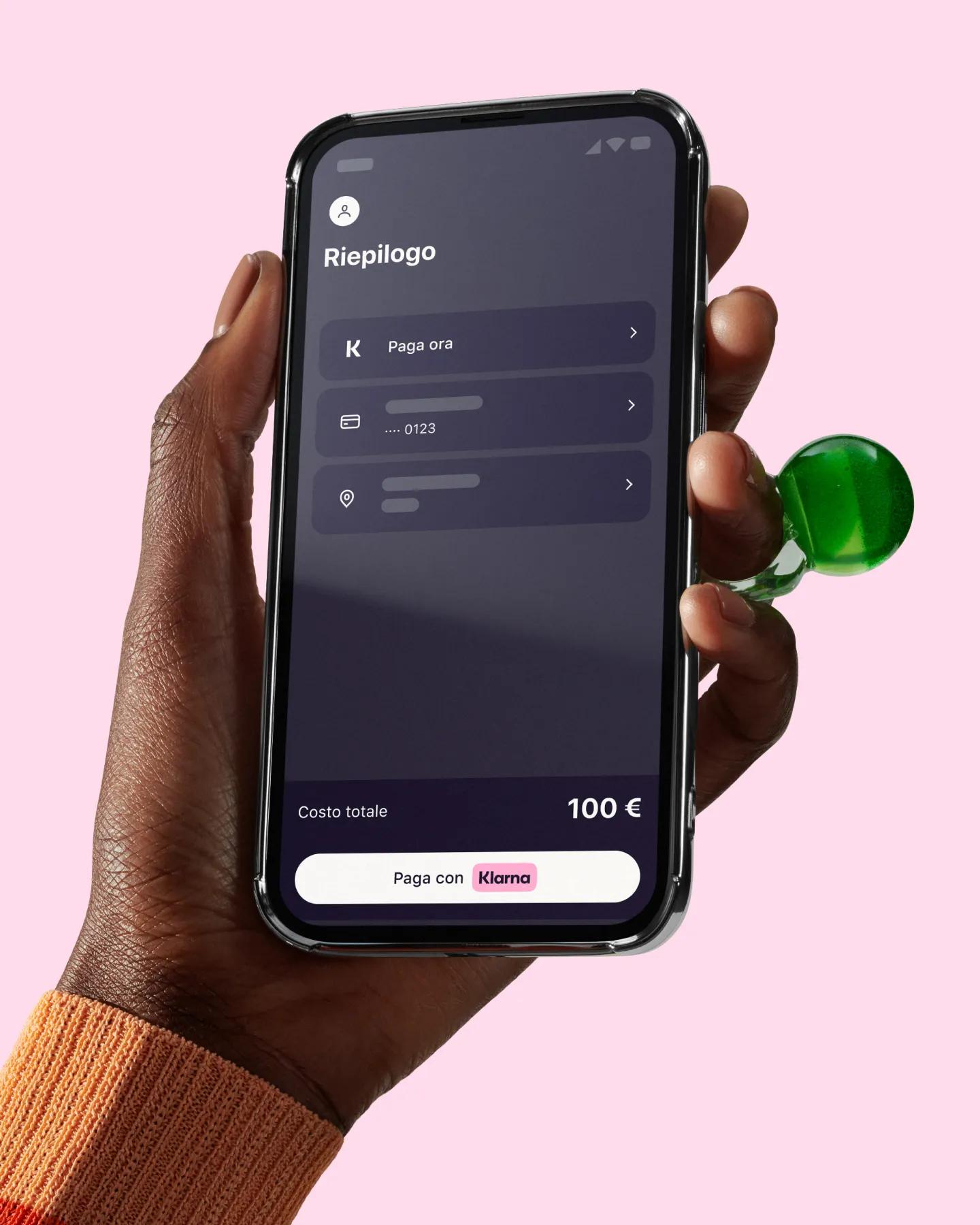Hand on a pink background holding a phone with Klarna app open