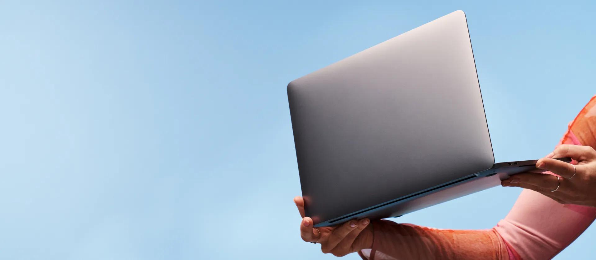 Two hands holding a silver laptop on a blue background