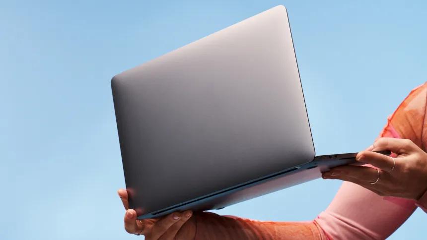 Two hands holding a silver laptop on a blue background