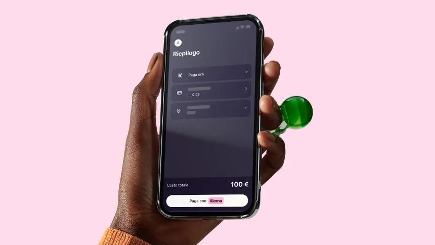 Hand on a pink background holding a phone with Klarna app open