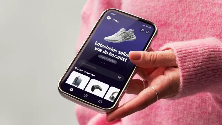 Hand holding a phone showing the Klarna app with pink sweater on background